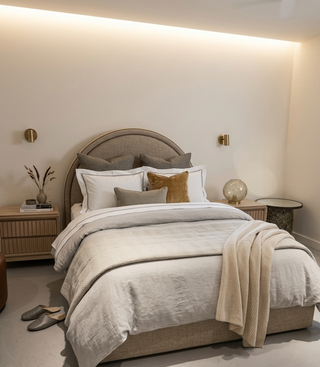 Neatly made bed with beige and white bedding in a modern bedroom setting.
