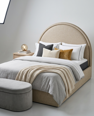 Beige upholstered bed with white bedding and decorative pillows in a minimalistic bedroom.