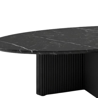 Modern oval dining table with a black marble-look top featuring white veining and a fluted black pedestal base, shown on a plain white background.